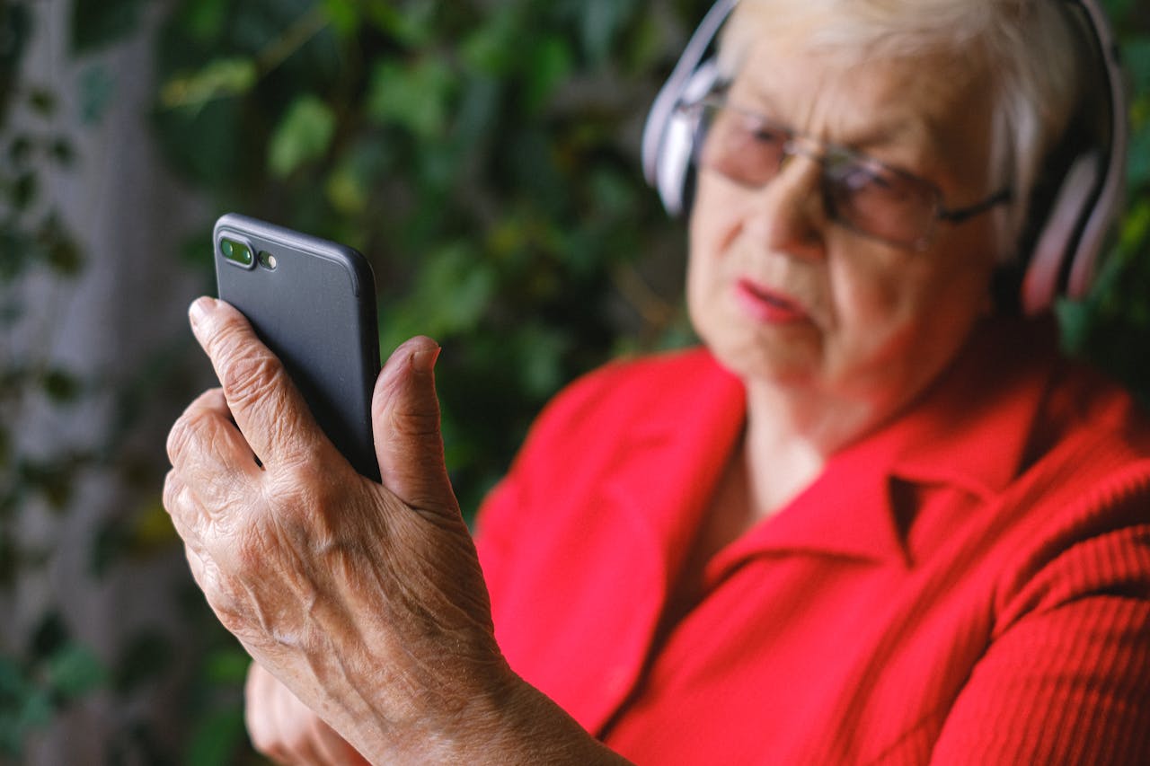 about-03 Senior woman in red using smartphone with headphones outdoors.