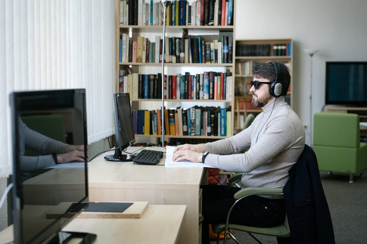 about-01 Man using Braille book with headphones in modern library setting.
